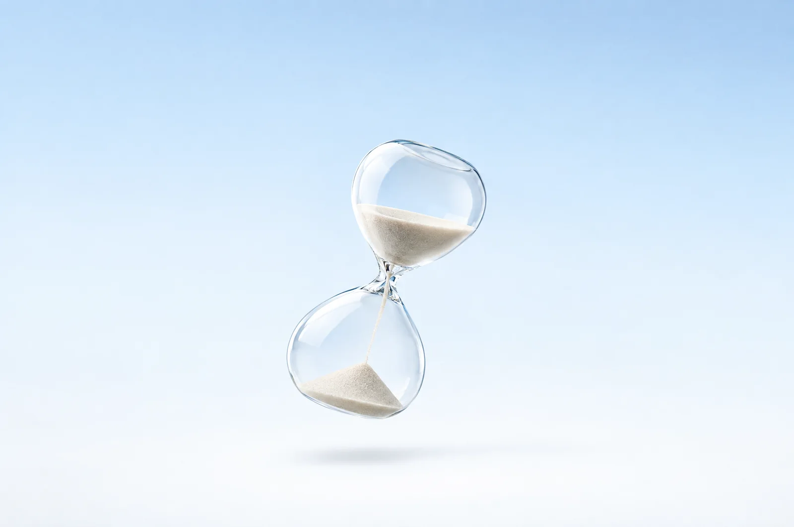 A glass hourglass on a pale blue surface